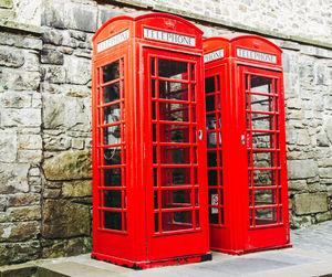 Red telephone booth on sidewalk against wall