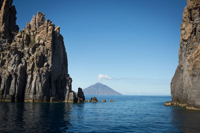 Panoramic view of rocks by sea against clear blue sky