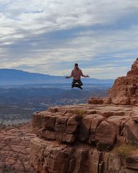 Full length of man levitating above rock against sky