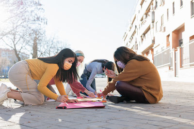 Females wearing mask drawing on banner on street