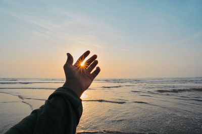 Cropped hand of woman using mobile phone at beach against sky during sunset