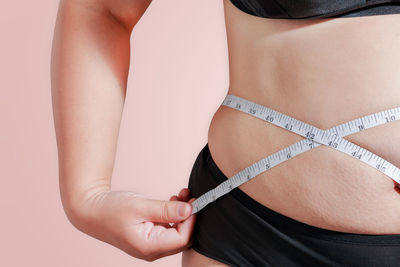 Midsection of woman measuring abdomen against colored background