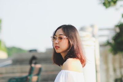 Side view of young woman wearing sunglasses standing against sky