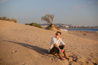 Young woman sitting on sand at beach against sky