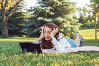 Young woman using phone while relaxing on grass
