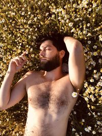 Directly above shot of shirtless man lying on plants outdoors