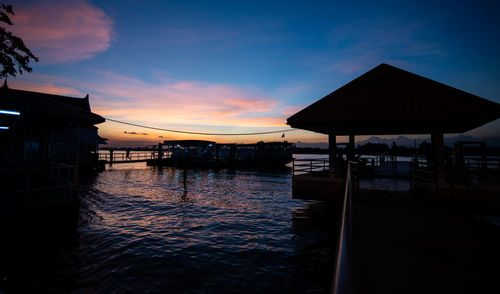 Silhouette swimming pool by sea against sky during sunset