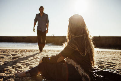 Man looking at woman while walking on shore against clear sky