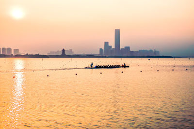 People riding boat on river by city against sky during sunset