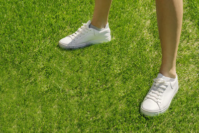 Female legs in white sneakers on a background on a green sports field. white sneakers for running