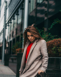 Young woman looking away while standing against built structure