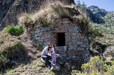 Mother with daughter sitting on rock against built structure