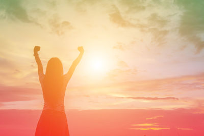 Silhouette woman with arms raised standing against sky during sunset