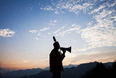 Silhouette man speaking on megaphone while standing against sky during sunset