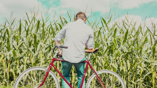 Rear view of woman standing on bicycle against sky