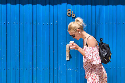 Full length of woman standing against blue metallic wall