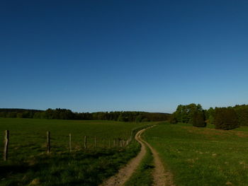 Dirt road amidst field against clear blue sky