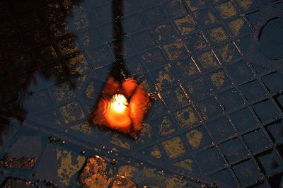 Reflection of illuminated street light on puddle at dusk