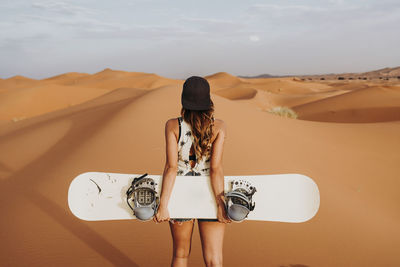 Back view of young female walking on sand and preparing for sandboarding looking away