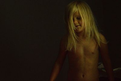 Shirtless girl with blond hair standing in darkroom