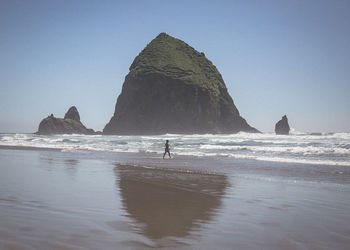 Man standing on rock by sea against clear sky