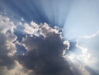 Low angle view of sunlight streaming through clouds