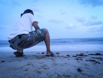 Full length of man crouching on beach against sky at dusk