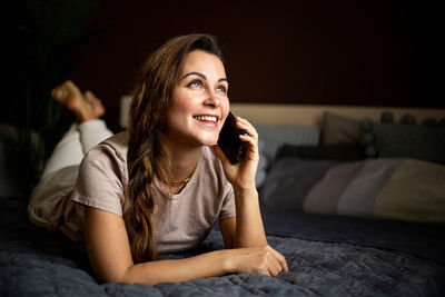 Smiling woman talking on phone while lying on bed