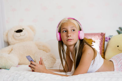Beautiful teenage girl is relaxing in bed using a touchscreen smartphone, listening to music
