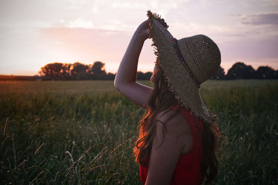 Rear view of woman standing on field at sunset