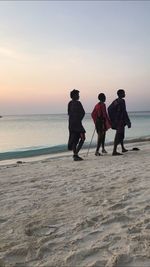 People walking on beach against sky during sunset