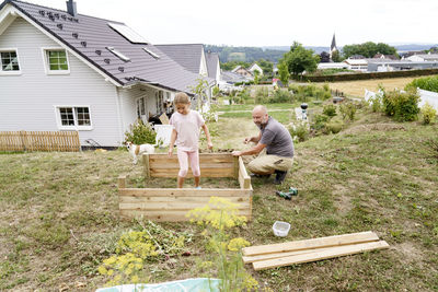 Father making raised bed with daughter in backyard near house