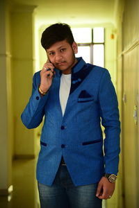 Portrait of young man talking mobile phone while standing in corridor