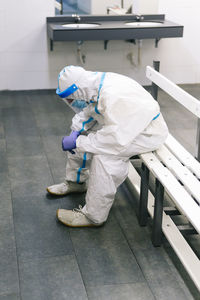 Contemplating man wearing protective suit sitting on bench in hospital