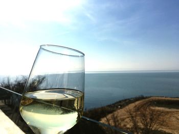 Glass of water by sea against sky