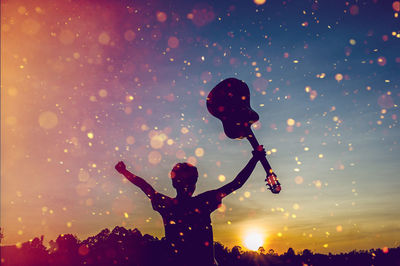 Silhouette man with arms raised standing against sky during sunset