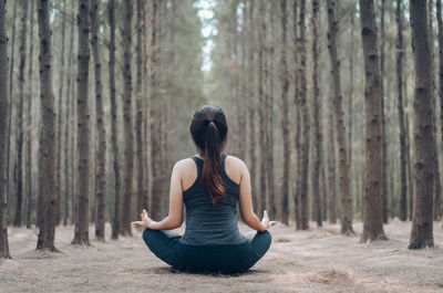 Rear view of woman practicing yoga in lotus position at forest