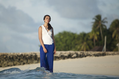 Young woman standing at beach against sky during sunset