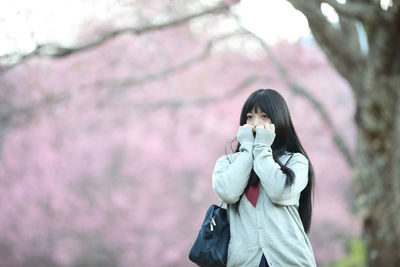 Young woman looking away while standing against pink flowering tree