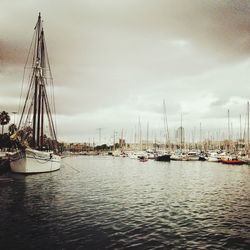 Boats in harbor against cloudy sky