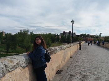 Portrait of woman standing by retaining wall against sky