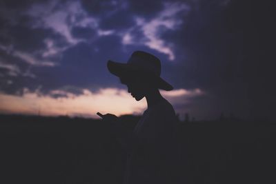 Silhouette woman using phone on field against sky during sunset