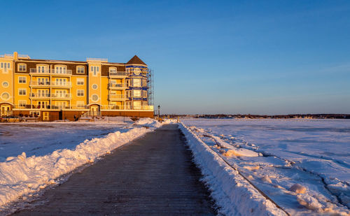 Snow covered road amidst buildings against sky