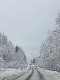 Road amidst snow covered trees against sky