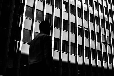 Rear view of silhouette man standing by building in city