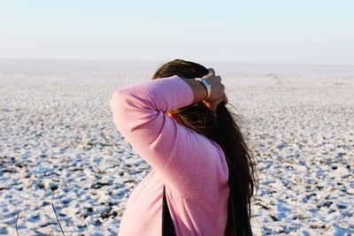 Rear view of young woman standing at beach against clear sky