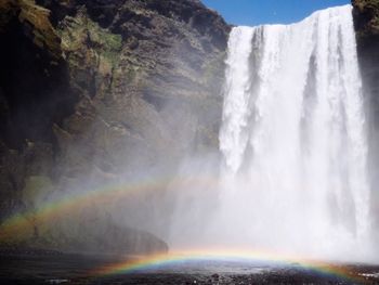 Scenic view of waterfall against rainbow in sky