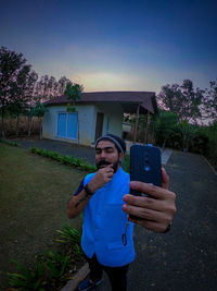 Portrait of young man photographing while standing against sky