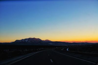 Road by mountains against clear sky during sunset