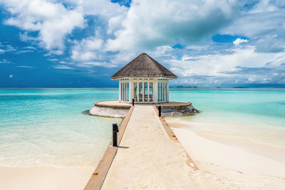 Scenic view of beach hut in maldives with turquoise water and dramatic sky